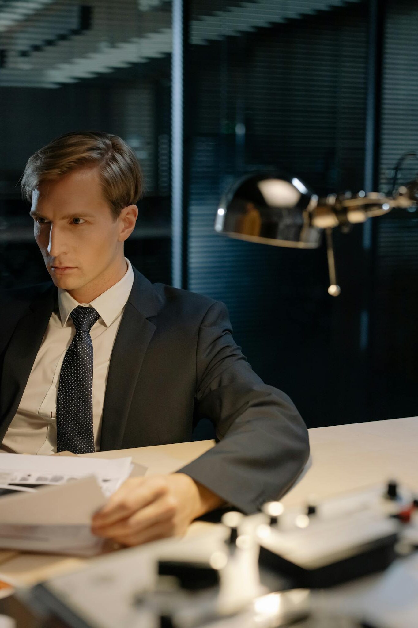 A focused investigator examines documents at a dimly lit office desk for crucial evidence.
